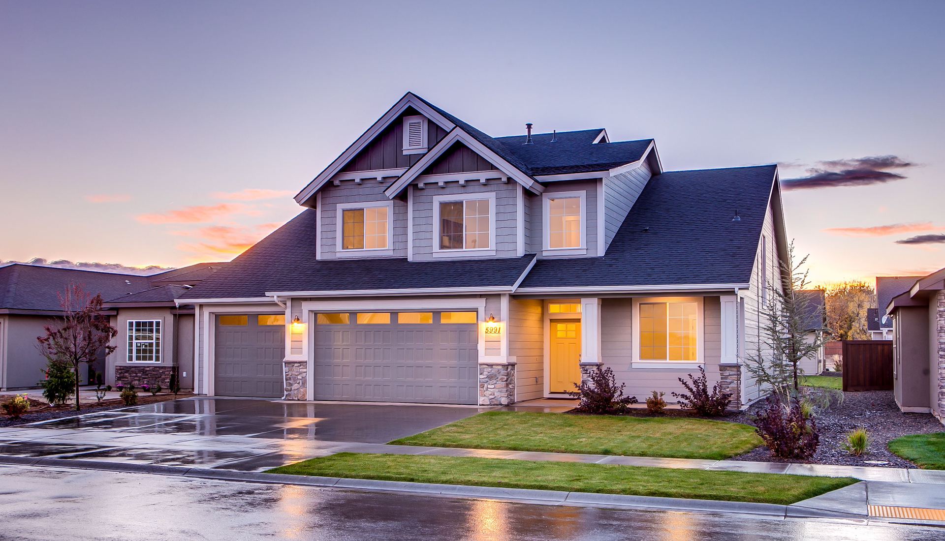 A two-story gray house with a three-car garage at dusk